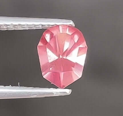 Pink gemstone held by tweezers against a dark background
