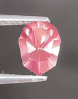 Pink gemstone held by tweezers against a dark background