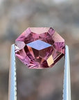 Pink gemstone held between tweezers with a blurred background