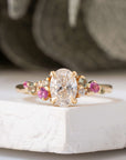 Gold ring with a central diamond and pink gemstones on a white surface