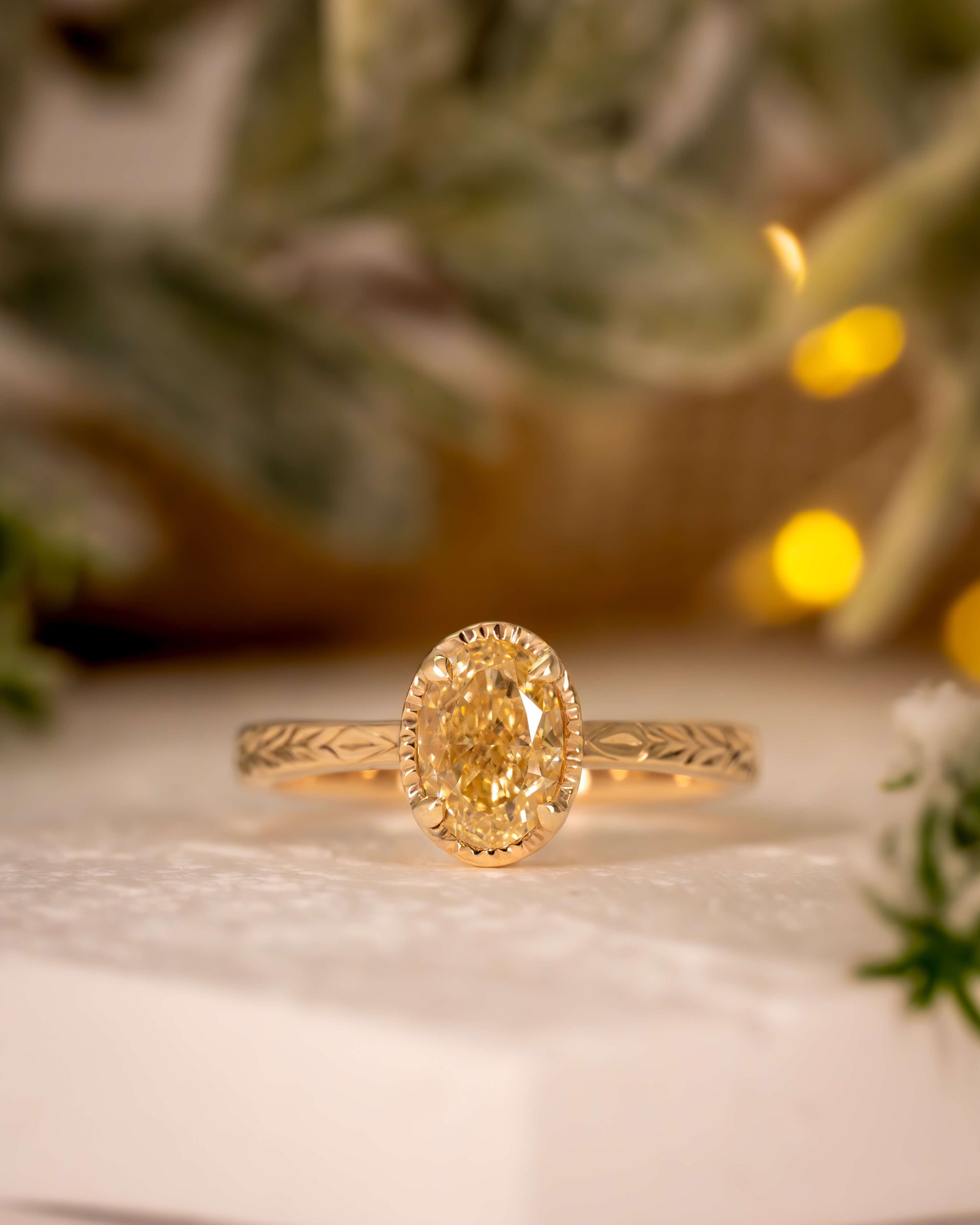 Gold ring with a diamond on a white surface with blurred greenery in the background