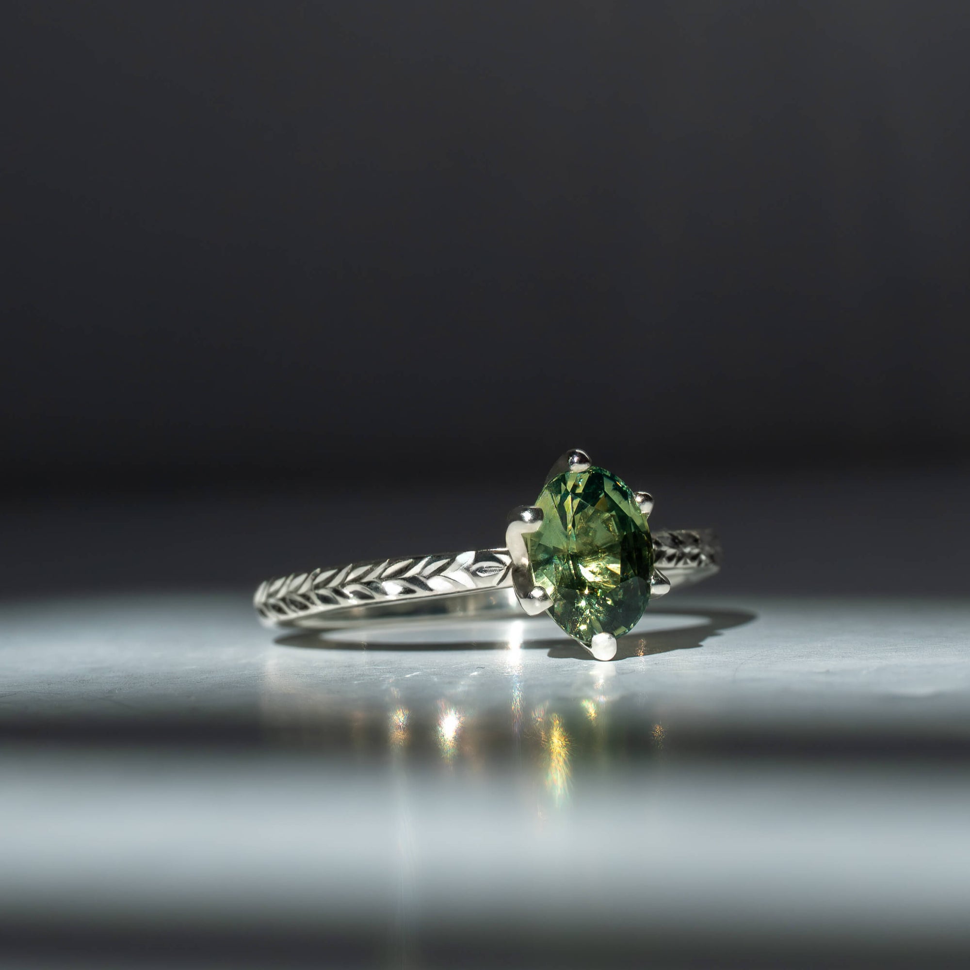 Silver ring with a green gemstone on a reflective surface with a dark background