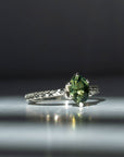 Silver ring with a green gemstone on a reflective surface with a dark background