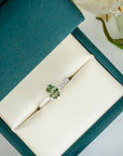 Silver ring with a green gemstone in a teal jewelry box with white flowers in the background
