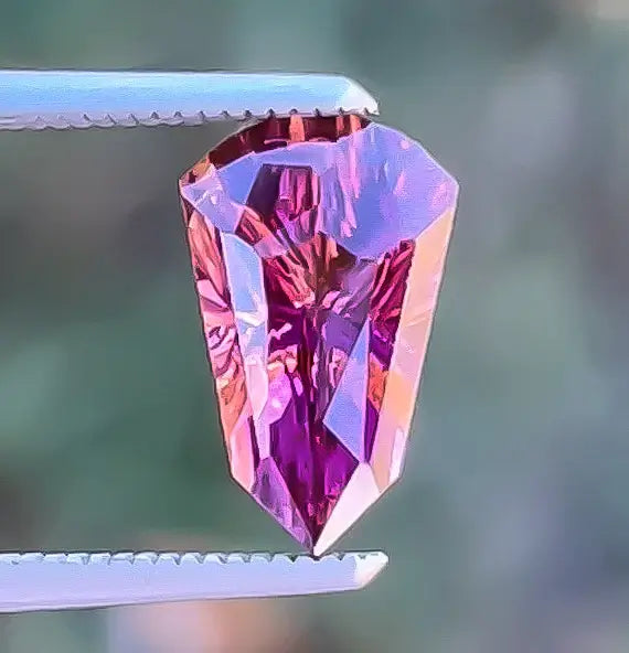 Faceted gemstone held by tweezers against a blurred green background