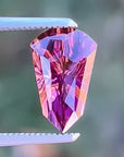 Faceted gemstone held by tweezers against a blurred green background